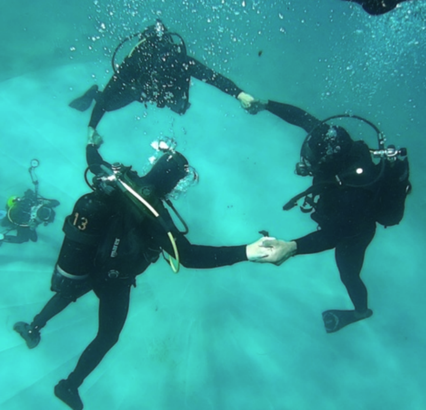Three scuba divers holding hands to make a triangle under the ocean